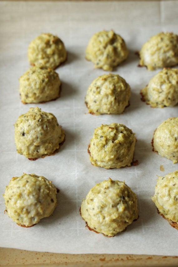 These juicy Pesto Chicken Meatballs are packed with fresh basil flavor, plenty of Parmesan cheese, and come together with just a handful of simple ingredients. They're baked instead of fried and ready in about 30 minutes making them an easy weeknight dinner or meal prep and packed with protein! Baked chicken meatballs on a sheet pan lined with paqrchment paper.
