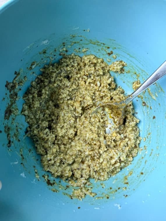 These juicy Pesto Chicken Meatballs are packed with fresh basil flavor, plenty of Parmesan cheese, and come together with just a handful of simple ingredients. They're baked instead of fried and ready in about 30 minutes making them an easy weeknight dinner or meal prep and packed with protein! Pesto and breadcrumbs mixed in a blue mixing bowl for chicken meatballs