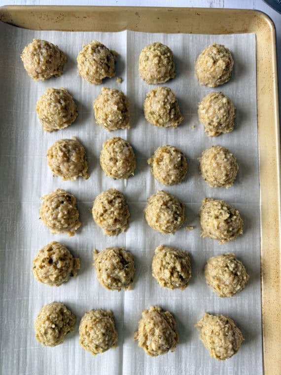 These juicy Pesto Chicken Meatballs are packed with fresh basil flavor, plenty of Parmesan cheese, and come together with just a handful of simple ingredients. They're baked instead of fried and ready in about 30 minutes making them an easy weeknight dinner or meal prep and packed with protein! raw chicken meatballs on a baking tray lined with parchment paper.