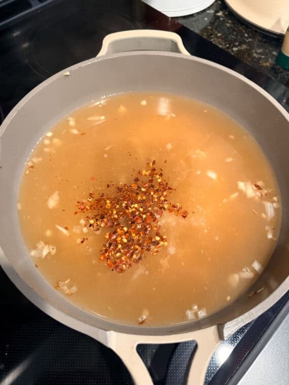 Adding spices into a skillet with broth.