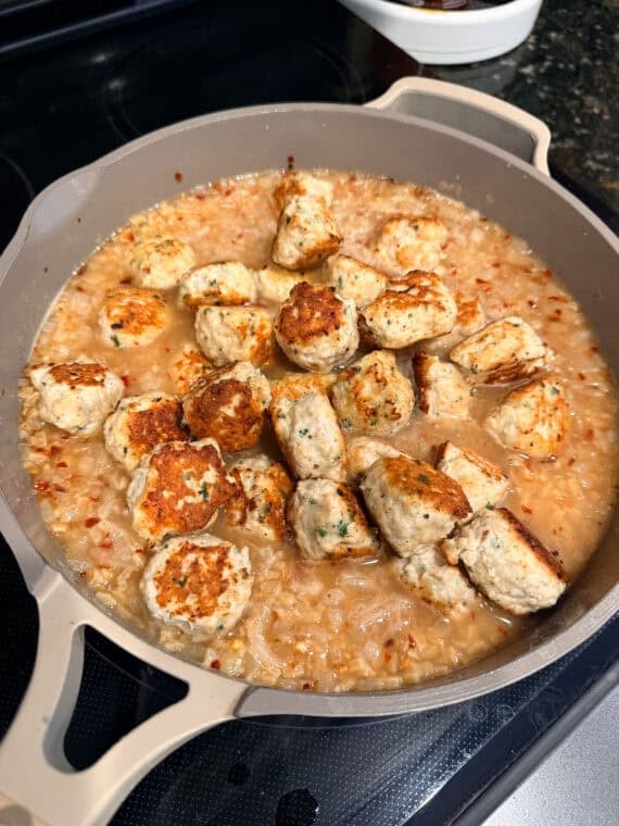Adding meatballs into a skillet with orzo past and broth.