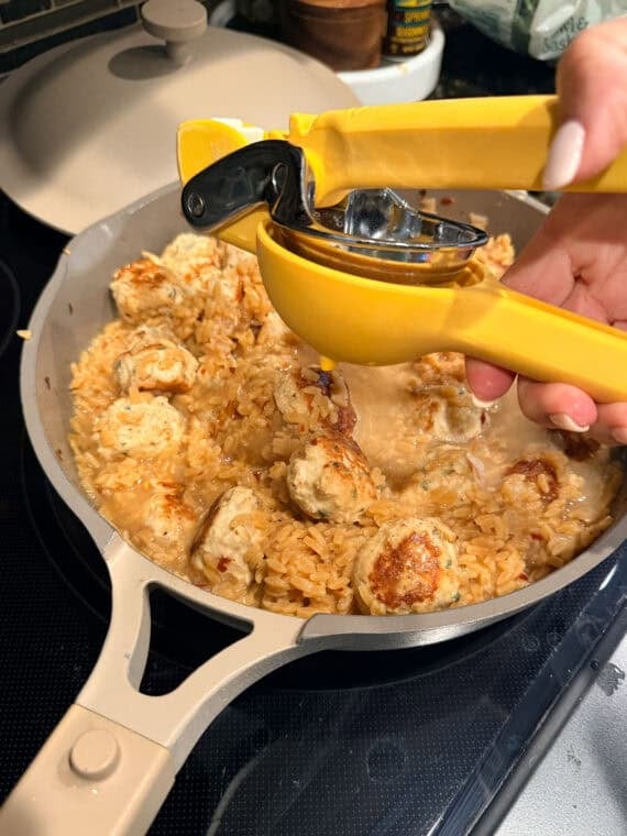 Squeezing lemon juice into a skillet with chicken meatballs and orzo pasta.