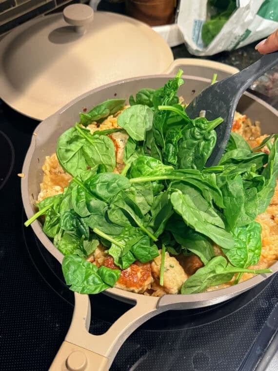 Adding fresh spinach into a skillet.