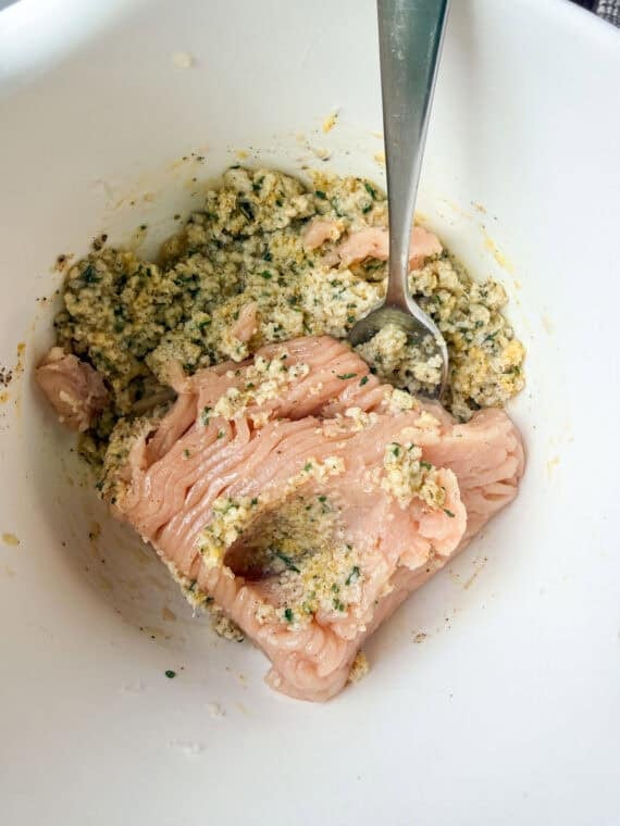Adding ground chicken into a bowl with soaked breadcrumbs for meatballs.