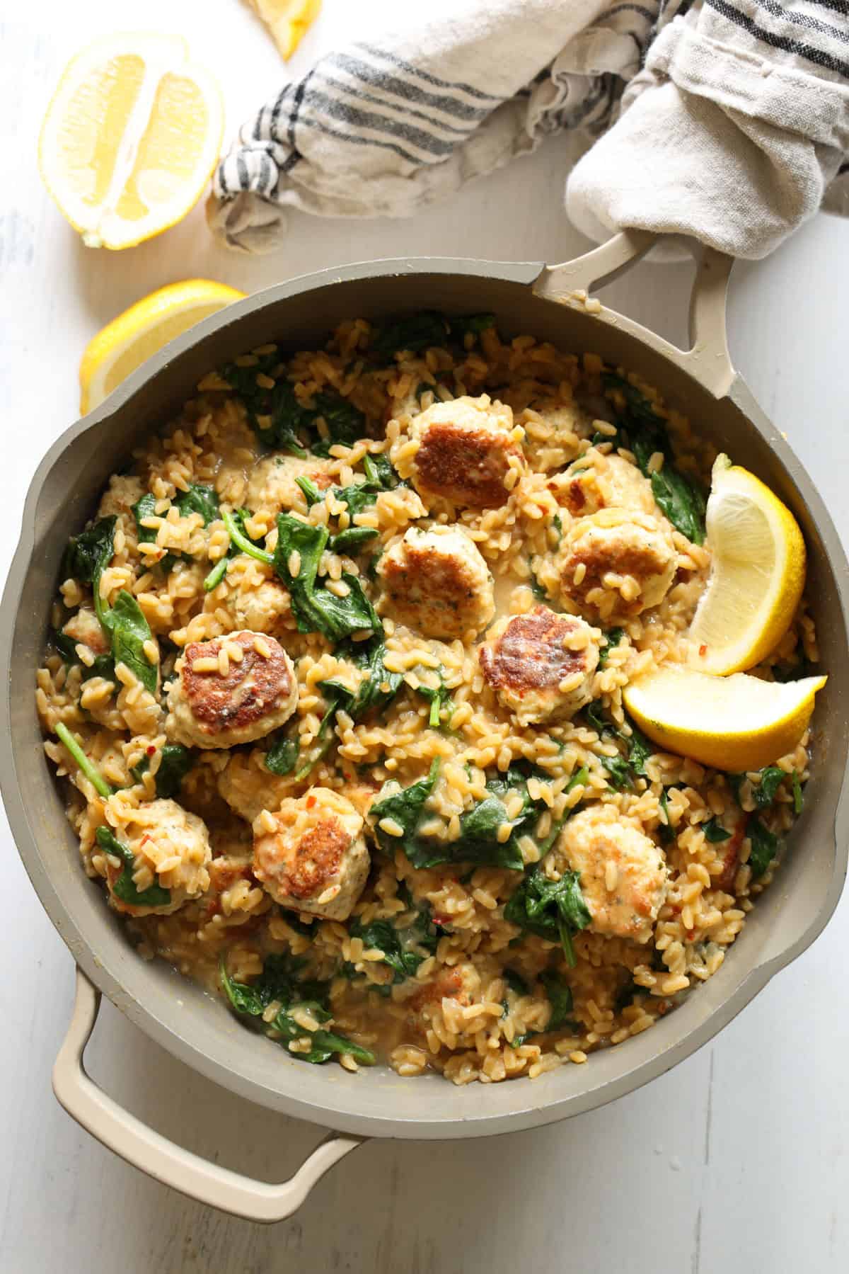 This High Protein Chicken Meatball Lemon Orzo Skillet is an easy one-pan dinner made with the juiciest chicken meatballs, creamy lemon orzo, fresh spinach, and Parmesan. The best part is each serving packs over 50 grams of protein! Lemon orzo in a skillet with chicken meatballs and a wooden serving spoon in the skillet