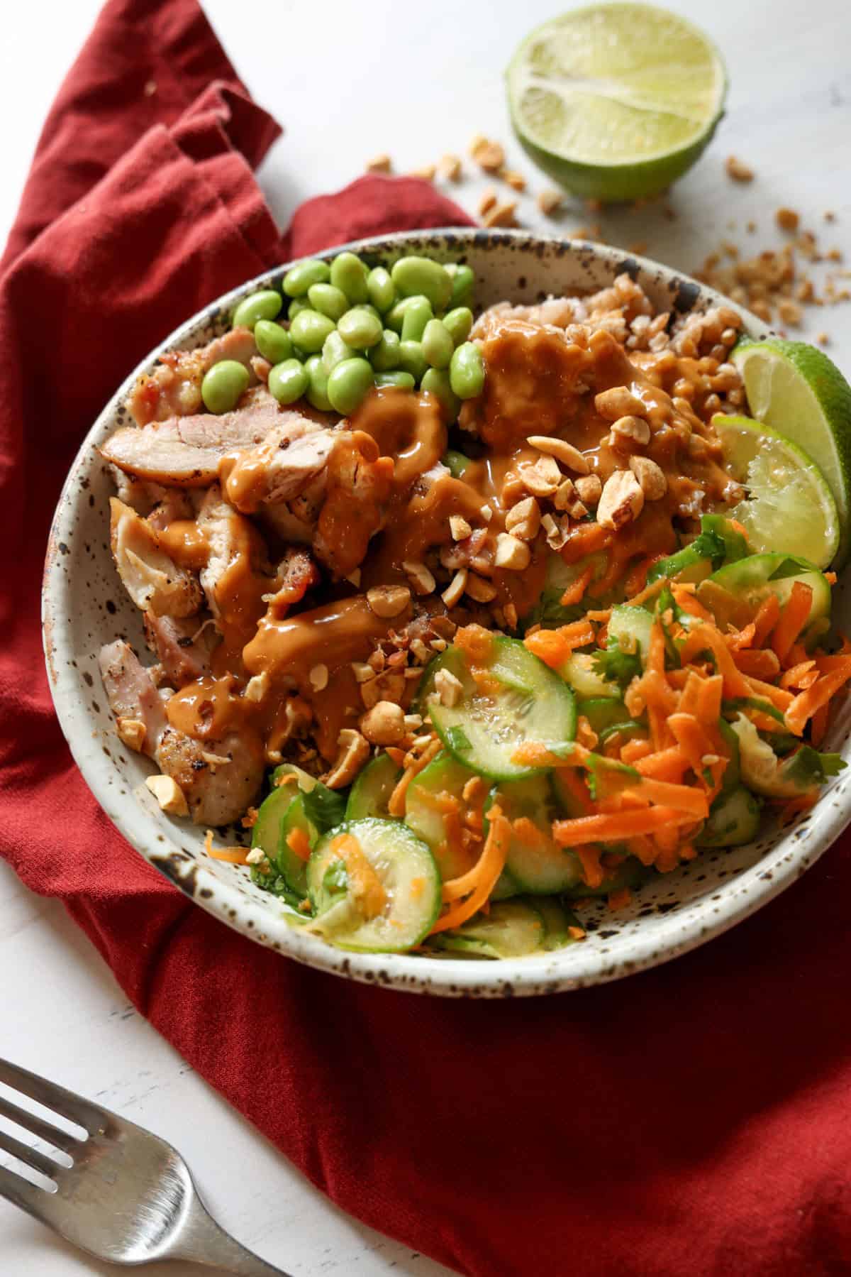 A prepared chicken bowl with peanut sauce, edamame, limes and chopped peanuts.