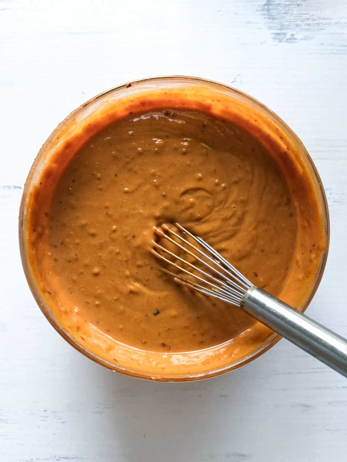 A spicy peanut sauce whisked together in a glass bowl