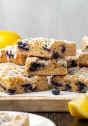 Lemon blueberry blondies stacked on a wooden cutting board.