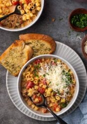 Overhead view of creamy Italian sausage soup in a bowl with a spoon, garnished with grated parmesan cheese, next to slices of garlic bread on a plate.