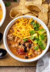 Overhead view of a bowl of creamy taco soup topped with shredded cheese and diced avocado.