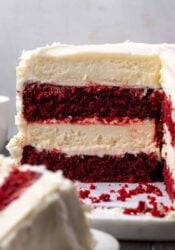 Side view of a red velvet cheesecake with a large slice missing, revealing the cake and cheesecake layers.