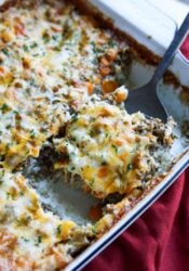 Cheese topped rice and ground beef casserole baked in a white ceramc baking dish with a spoon serving a piece