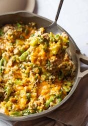 A spoon scooping cheesy chicken and broccoli with rice from a skillet.