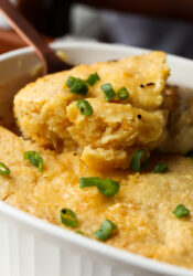 A spoon scoops a serving of cornbread chicken casserole from a baking dish.