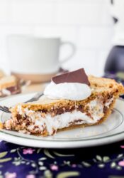 A slice of s'mores pie on a plate topped with marshmallow creme and a piece of chocolate