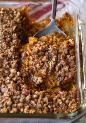 A serving spoon removing a scoop of sweet potato souffle from a baking dish.