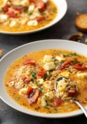 A bowl of Greek tomato feta soup with a spoon, and another bowl of soup in the background.