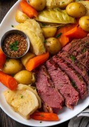 Overhead view of sliced corned beef on a plate next to cabbage, potatoes, and carrots.